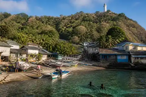 Apo Island village shoreline with beached boats, village houses and hilltop lighthouse
