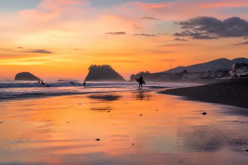 Sunrise on Sabang Beach, Baler with surfers and wet dark sand reflecting dawn light