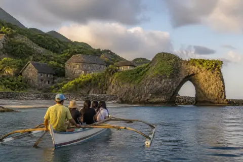 Faluwa boat approaching Nakabuang Arch and Ivatan stone houses on Sabtang
