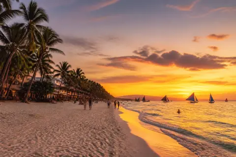 White Beach, Boracay at sunset with paraw sailboats and palm-fringed shoreline
