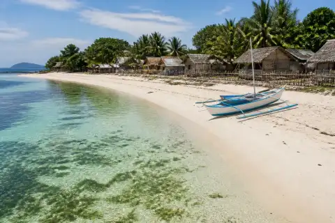 Pale-sand beach and shallow seagrass shore on Debangan Island with a small outrigger boat