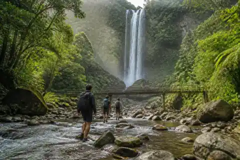 Trekkers crossing a river toward Ditumabo Mother Falls in a shaded Sierra Madre forest