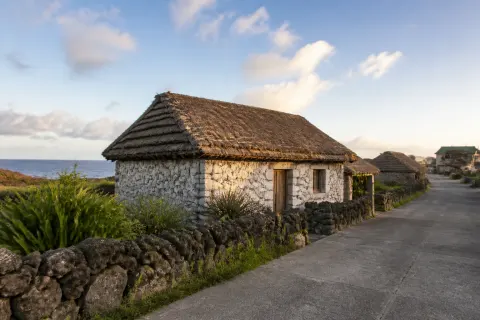 Low stone Ivatan house with thatched roof beside a village road in Ivana, Batanes
