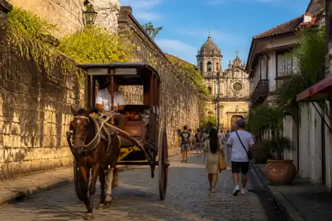 Cobbled street and colonial walls inside Intramuros with a horse-drawn kalesa and pedestrians