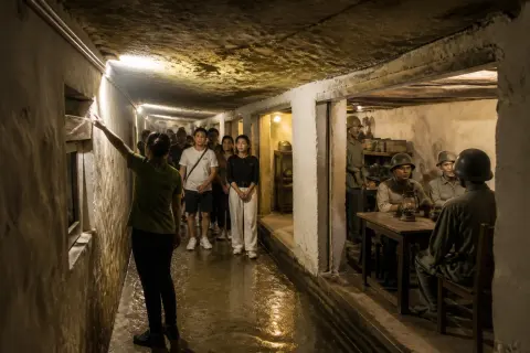 Narrow dim tunnel interior with low ceiling, wartime mannequins and a guide