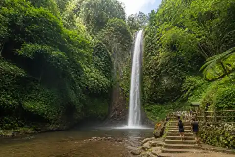 Tall single‑drop Katibawasan Falls plunging into a shallow pool with forested cliffs and viewing stairs