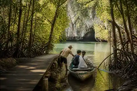 Mangrove boardwalk and paddleboat approaching limestone outcrop and cave at Lamanok Island, Anda