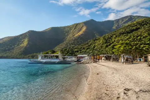 Masasa Beach shoreline with small passenger boats, a tricycle and island hills