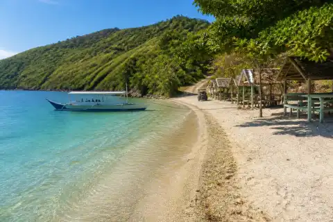 Masasa Beach shoreline with clear water, small passenger boat and island shade structures on Tingloy, Batangas