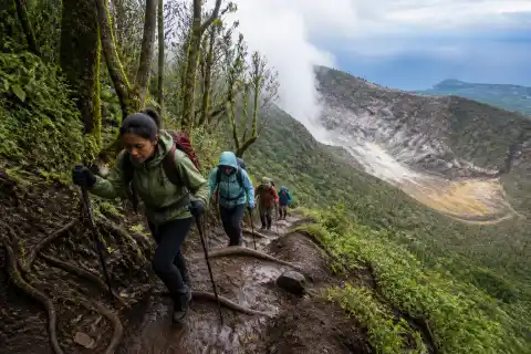 Hikers on a steep mossy trail on Mount Hibok-Hibok with cloudy upper slopes and distant sea