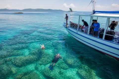 Snorkelers and an expedition boat over a shallow reef near Balabac