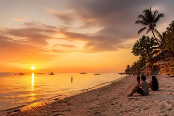 West-facing Panglao shoreline at sunset with silhouetted boats and low-rise resort frontage