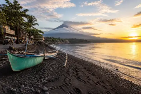 Sunrise over Santo Domingo black-sand beach with fishing boats and distant Mayon volcano