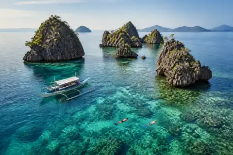 Snorkelers and a small boat beside limestone islets at Siete Pecados Marine Park, Coron