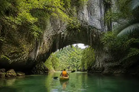 Kayak passing beneath a limestone natural bridge on a jungle river at Sohoton, Basey, Samar
