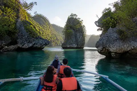 Small boat entering Sohoton Cove lagoon surrounded by limestone islets and green vegetation