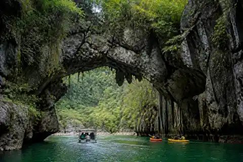 Kayaks and a boat approaching a limestone natural bridge over a rainforest river at Sohoton, Basey, Samar