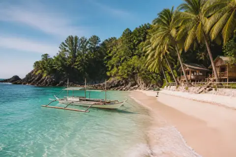 Pinkish-white sand cove at Subic Beach with an outrigger boat and cottages