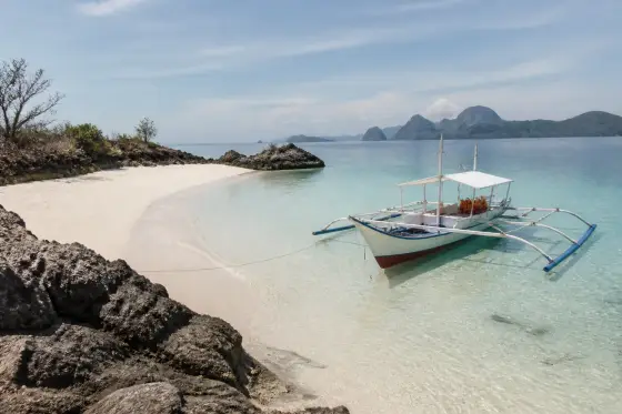 Small cream‑colored beach and rocky shore of Turtle Island, Guimaras, with a small island‑hopping boat