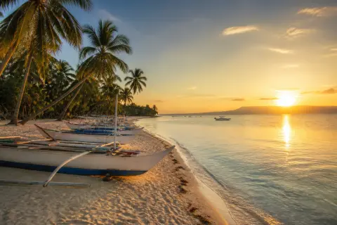 Panglao beach at sunset with bancas and palm trees