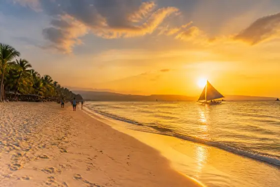 Sunset on Boracay's White Beach with a paraw sailboat and people walking along the shore