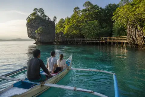 Small traditional boat approaching mangrove and limestone outcrop at Lamanok, Anda