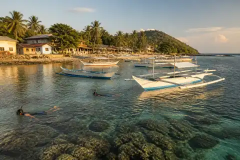 Apo Island shoreline with small boats and snorkelers near the coral reef