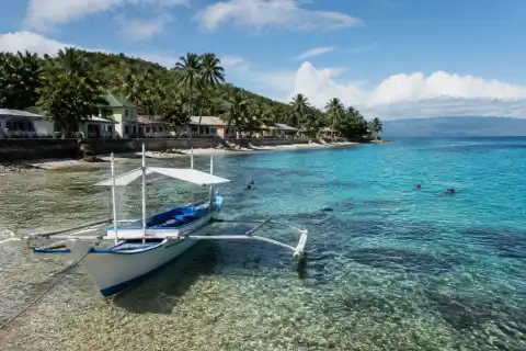 Apo Island shoreline with a small outrigger banca and snorkelers near the reef