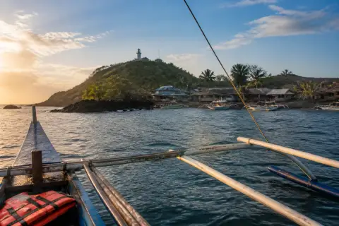 Boat approaching Apo Island volcanic shoreline with village and lighthouse