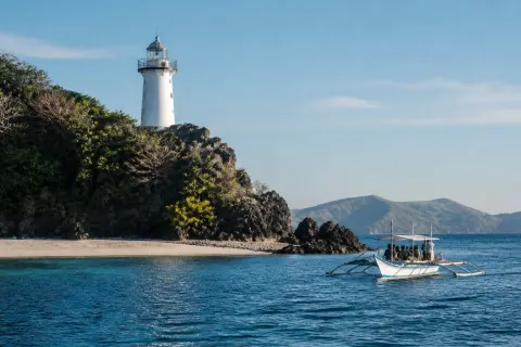 White iron lighthouse on Bagatao Island headland with a banca approaching Parola Beach