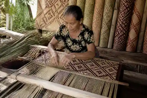 Artisan hand-weaving a tikog banig in a Basey workshop with dried sedge and finished mats