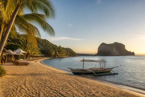 Batangas resort beach with a moored banca and distant limestone outcrop