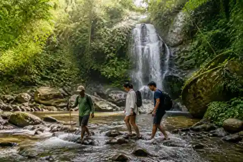 Travelers crossing a rocky stream toward a tropical waterfall in Iloilo