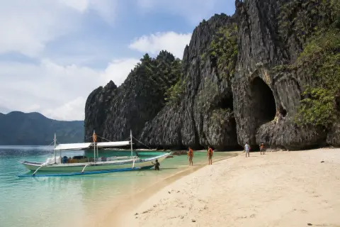 Pale sandy beach, dark limestone karst and a small anchored boat at Black Island (Malajon), Busuanga
