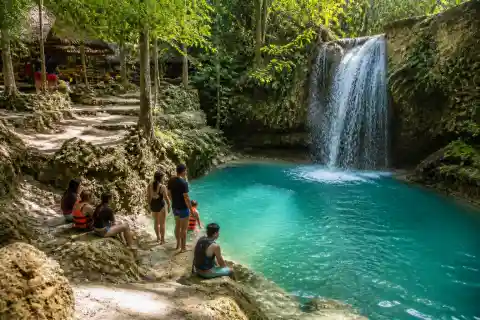 Visitors at a rocky freshwater waterfall pool in Bolinao with shaded trees and swim area