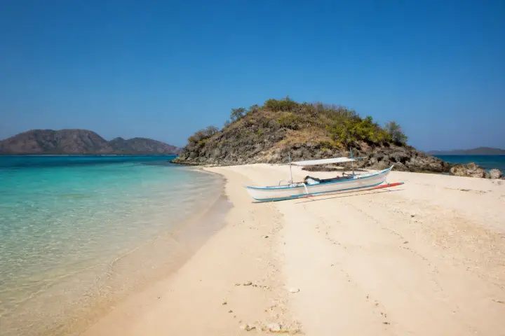 Sandbar and shallow turquoise water at Bulog Dos with a small outrigger boat