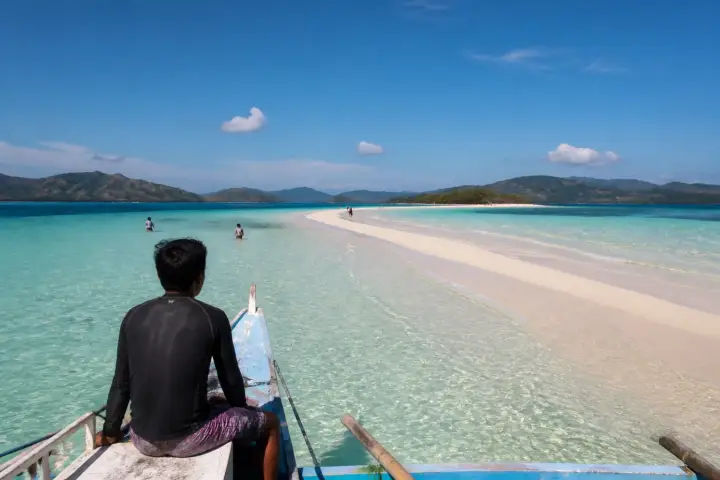 Small banca approaching a pale sandbar with swimmers near Culion, Palawan