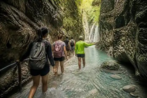 Guide-led group walking the turquoise canyon toward Dao Falls in Samboan