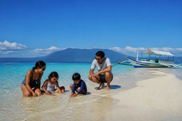 Family on the White Island sandbar in Camiguin with shallow turquoise water and a moored boat