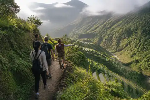 Travelers led by a local guide walking along a terrace path above Banaue rice terraces