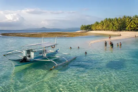 Banca anchored by a sandbar and sandy island in Honda Bay with swimmers in shallow turquoise water