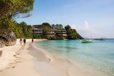 Ilig-Iligan Beach shoreline with pale sand, clear shallows and small boats in morning light