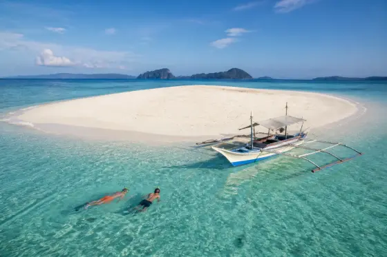Bright sandbar with a small banca and snorkelers in Taytay Bay, Palawan