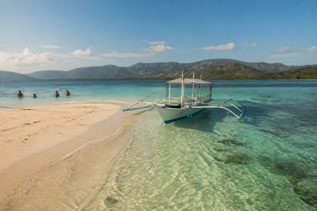 Outrigger boat by pale sandbar and snorkelers at Isla Blanca, Taytay Bay