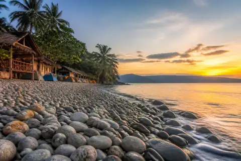 Pebble shoreline at Mabua Beach with cottages and sunset