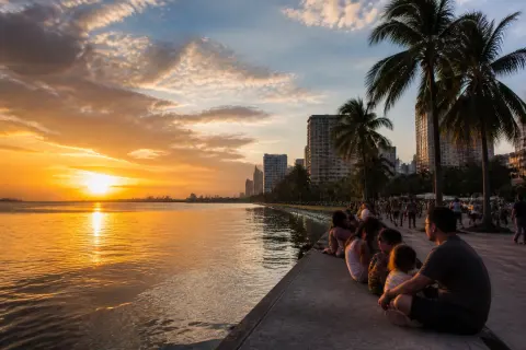 People watching sunset over Manila Bay from the Baywalk with palm trees and the waterfront promenade