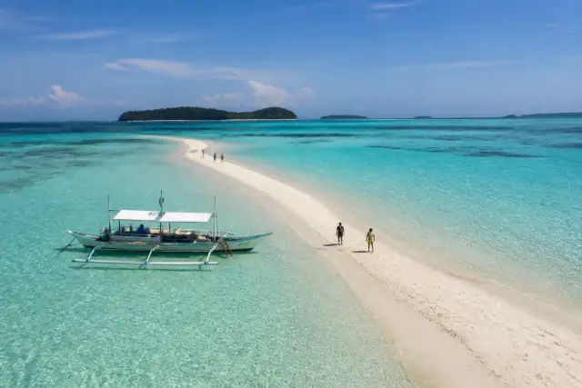 Mansalangan sandbar at low tide with shallow turquoise water and a small boat