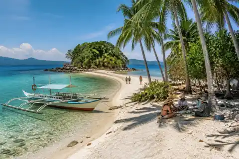 Coconut‑backed white sand beach at Maxima Island with a banca and visible sandbar