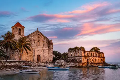 Oslob heritage waterfront at dusk with church, ruins and small boats