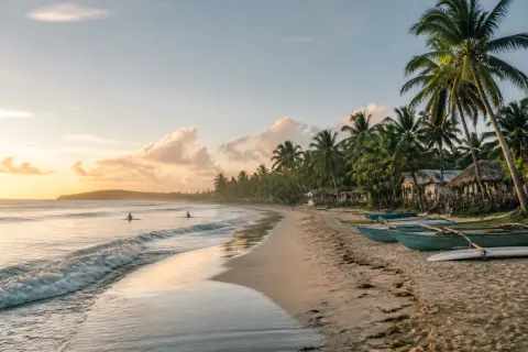 Sunrise surfers and palms along Pacifico Beach, north Siargao